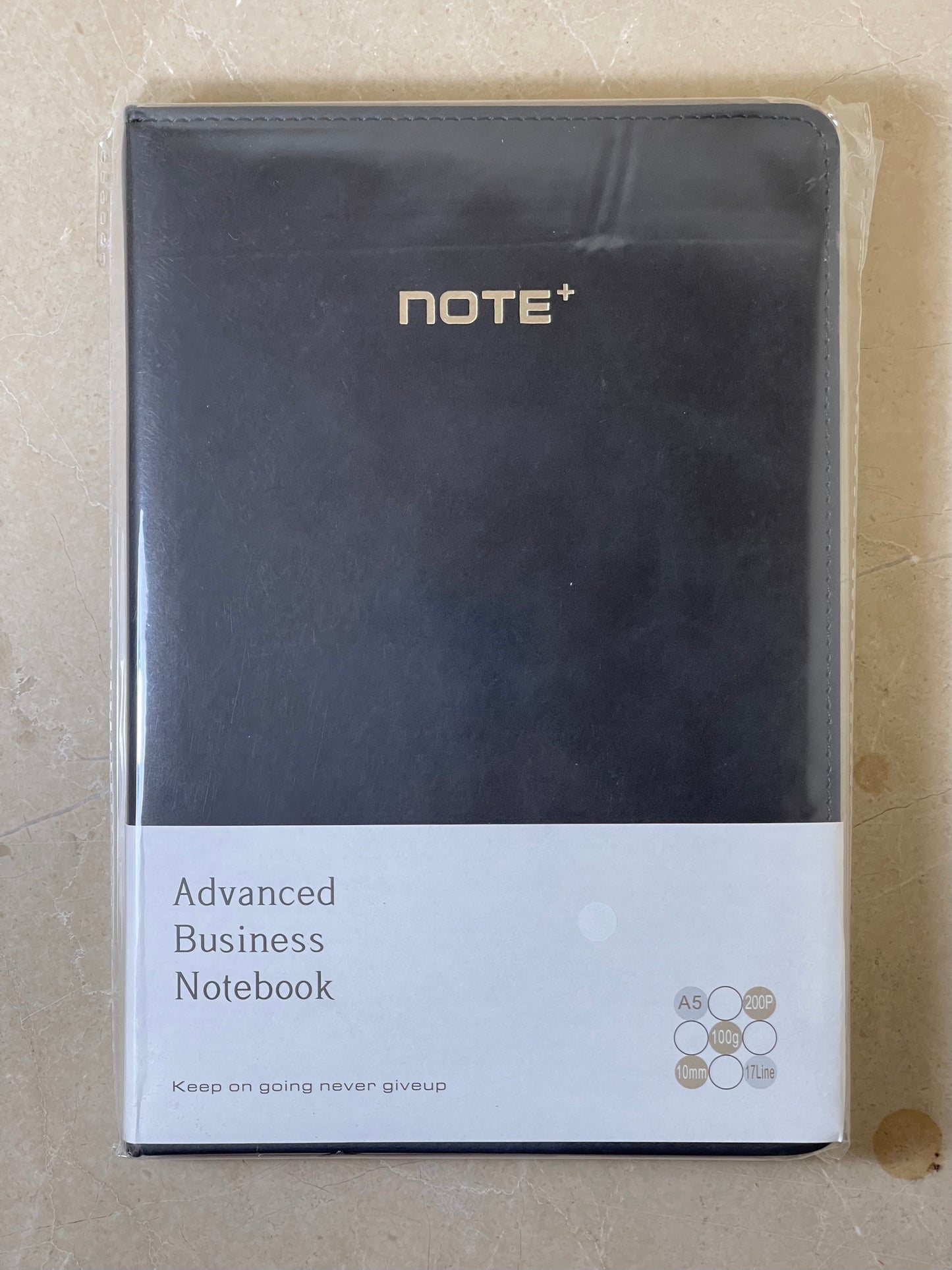 Black notebook with 'NOTE+' branding on a beige surface