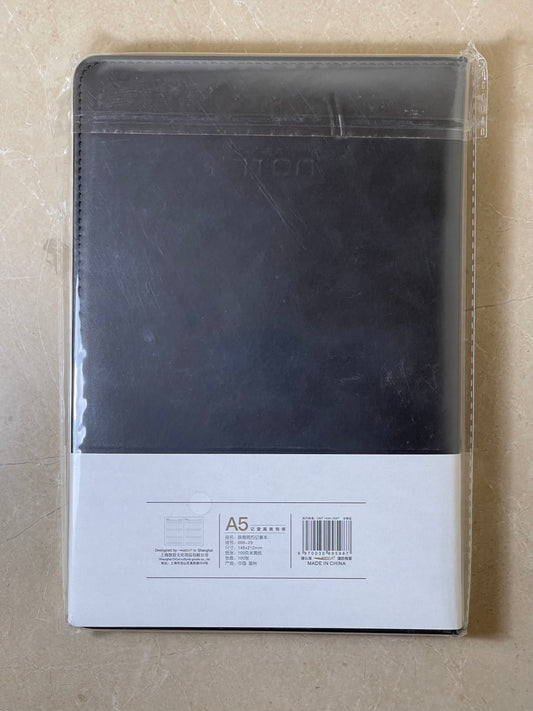 Black notebook in clear packaging on a beige background