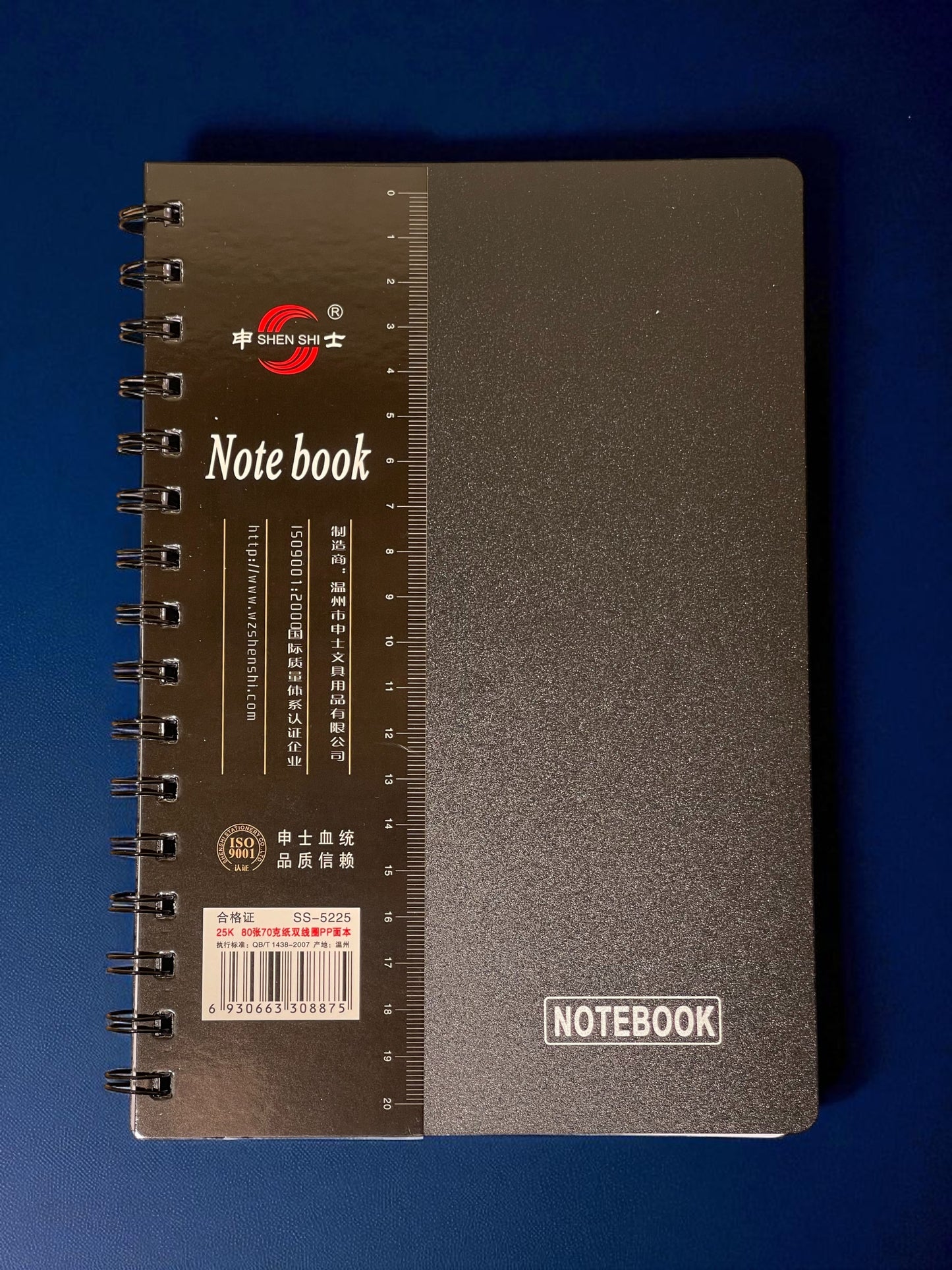 Black spiral notebook with brand logo on a blue background