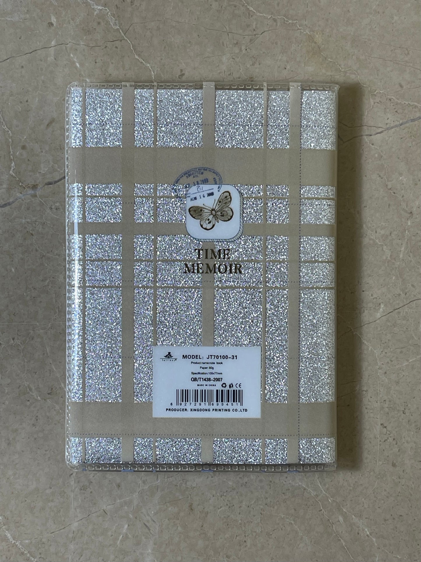 Notebook with glittery cover and butterfly design on a textured surface