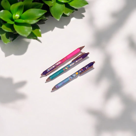 Three colorful pens on a light surface with a plant in the corner