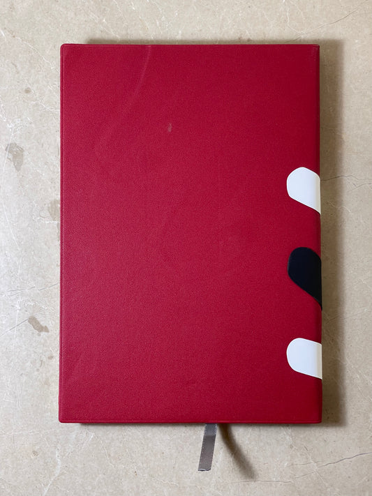 Red notebook with white and black design on a beige surface