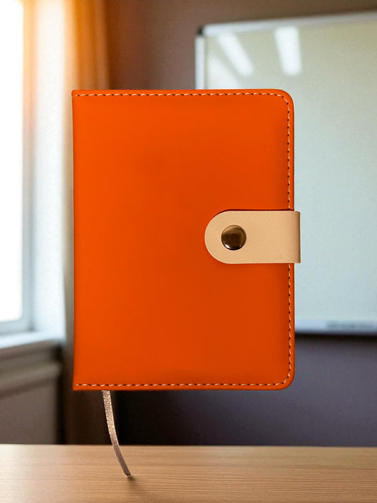 Orange leather notebook with a gold buckle on a wooden surface.