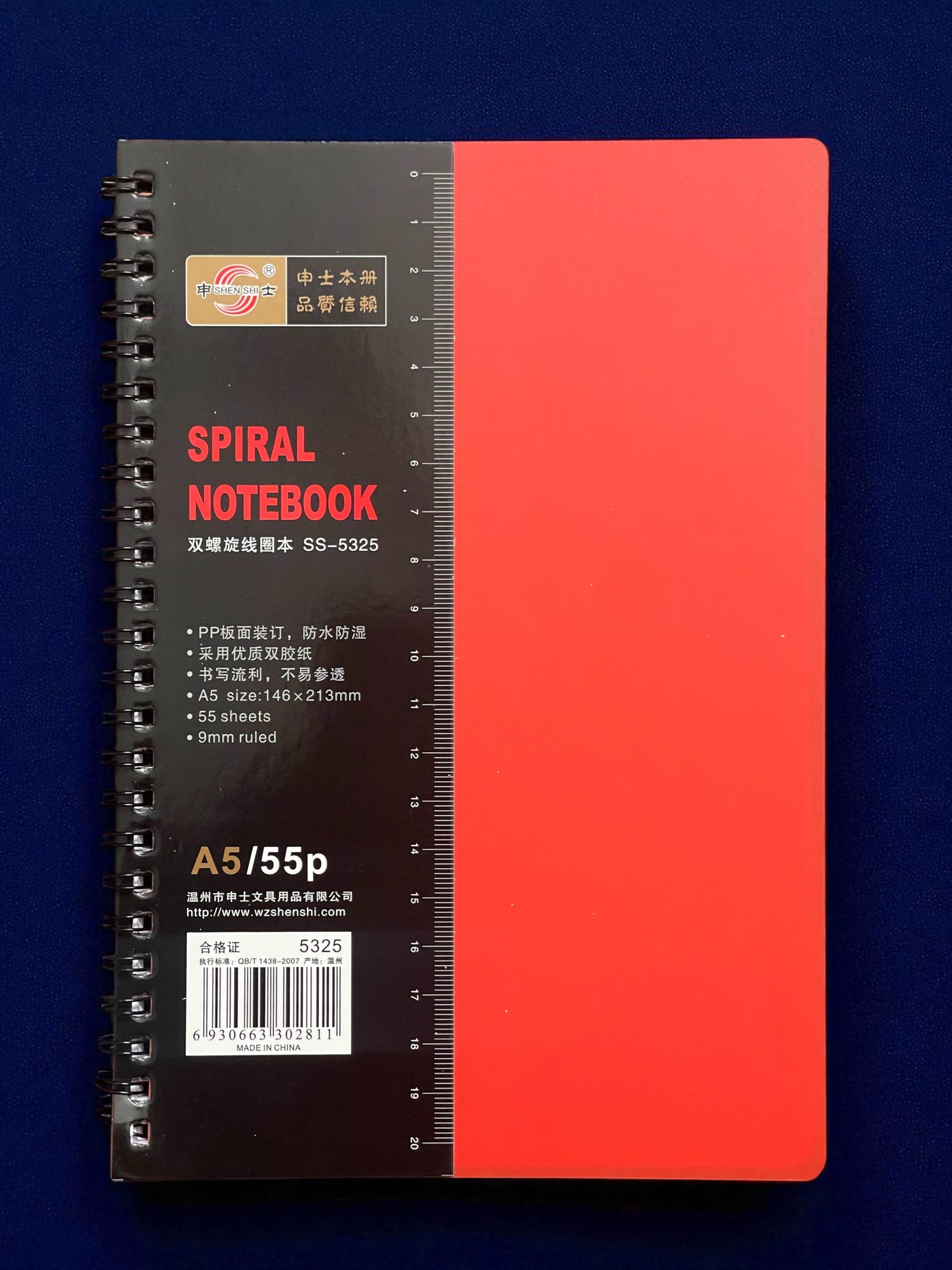 Spiral notebook with red cover and black back on a blue background