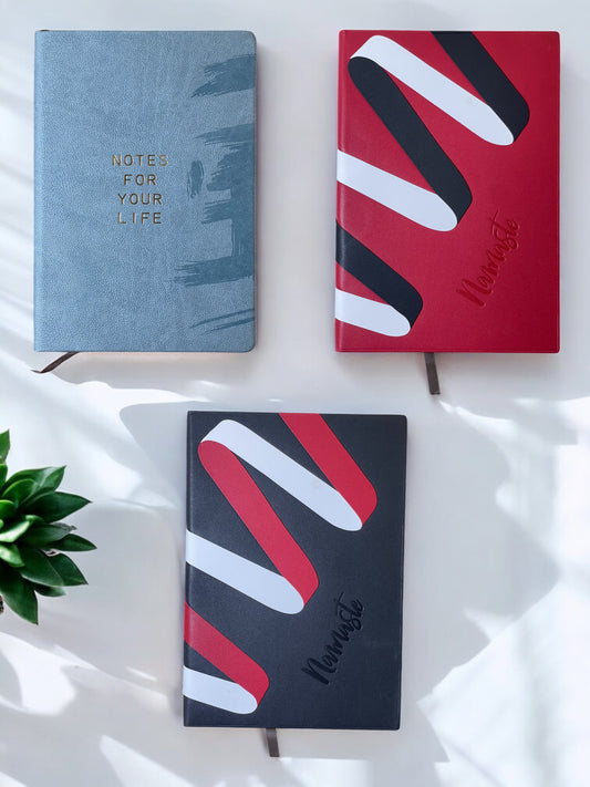 Three notebooks with different designs on a white surface with a plant.